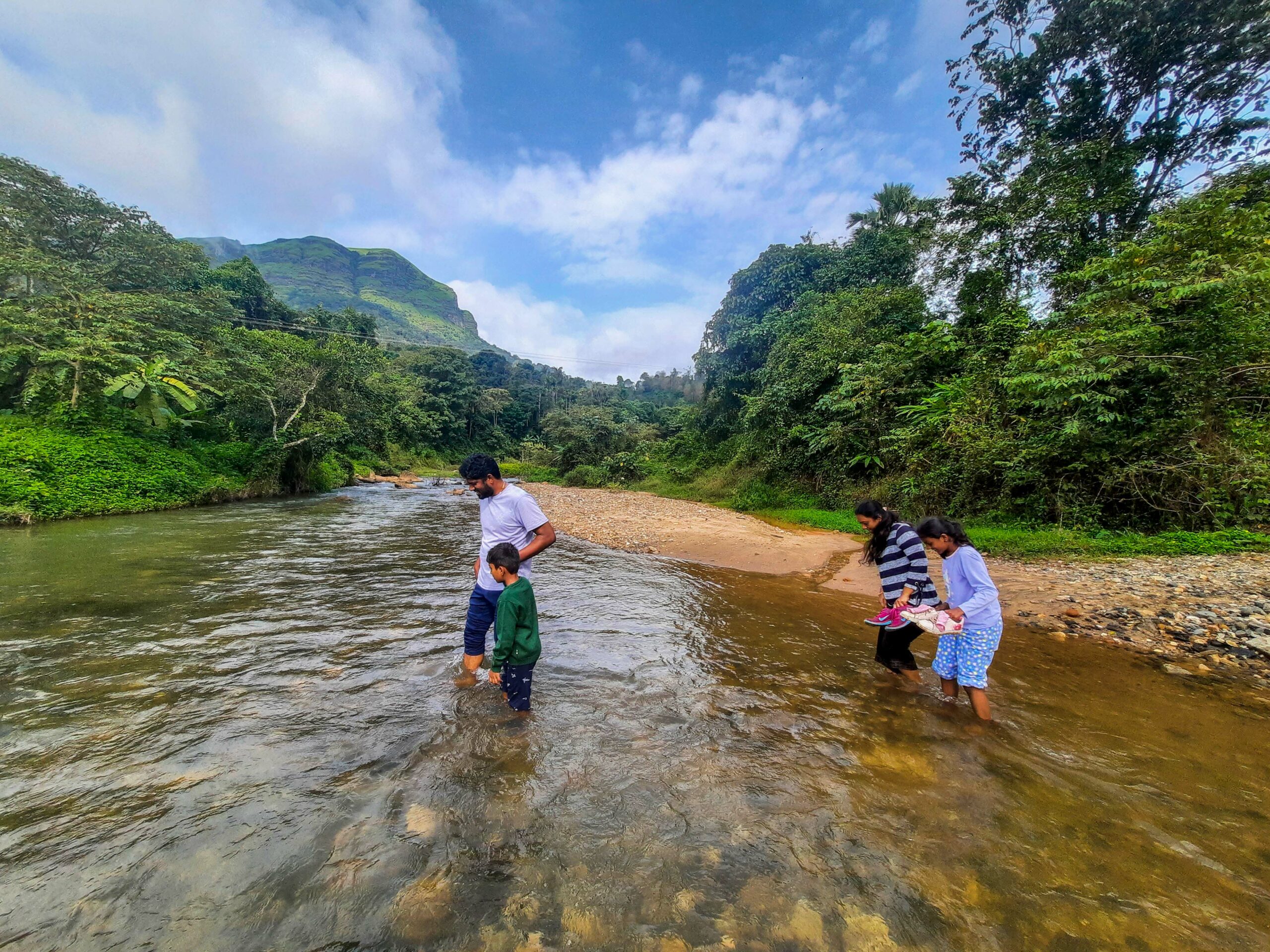 Family standing in shallow rocky river. RiverMist Resorts.