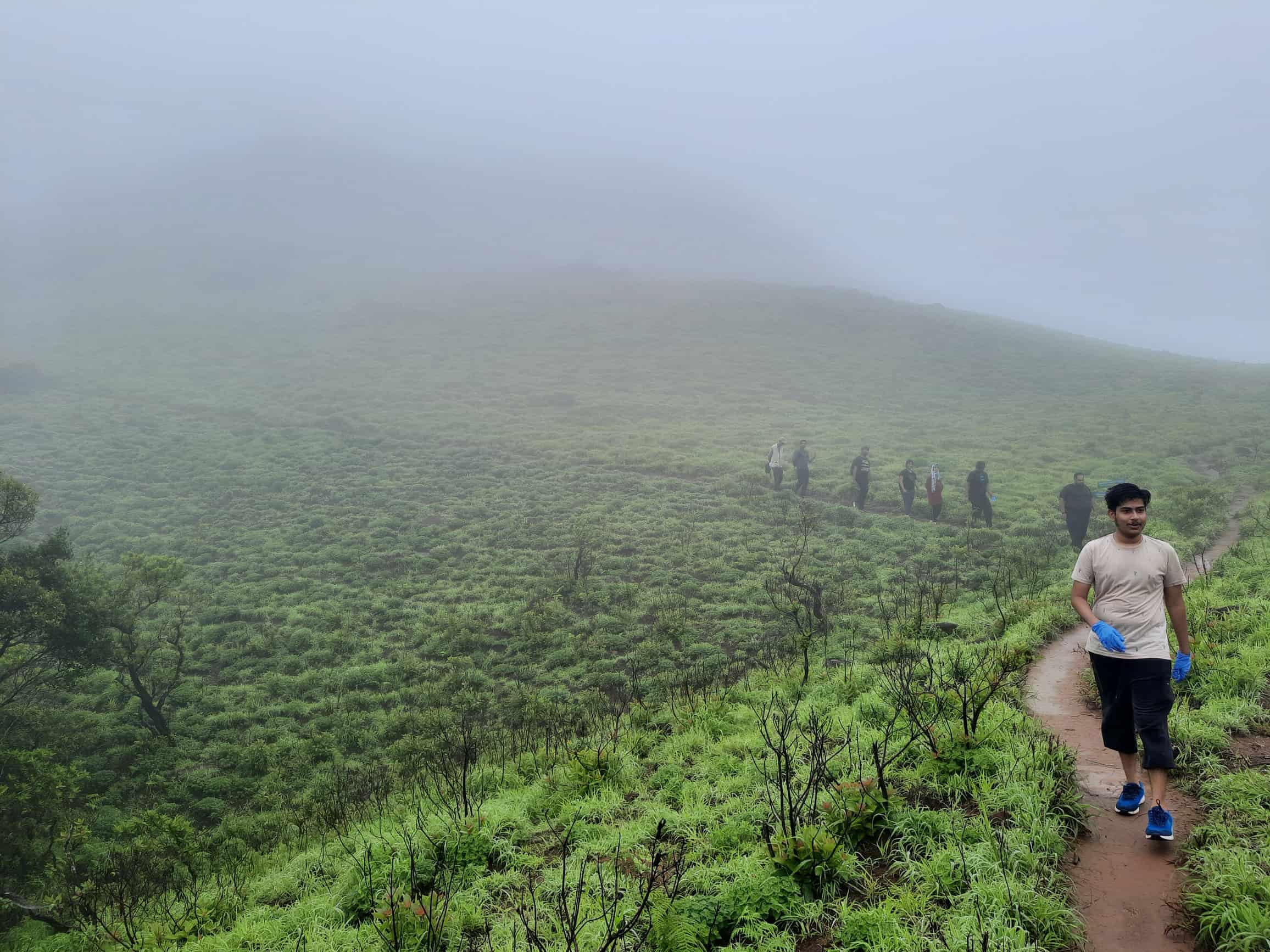 Hiker walking muddy trail on misty hillside. Western Ghats.
