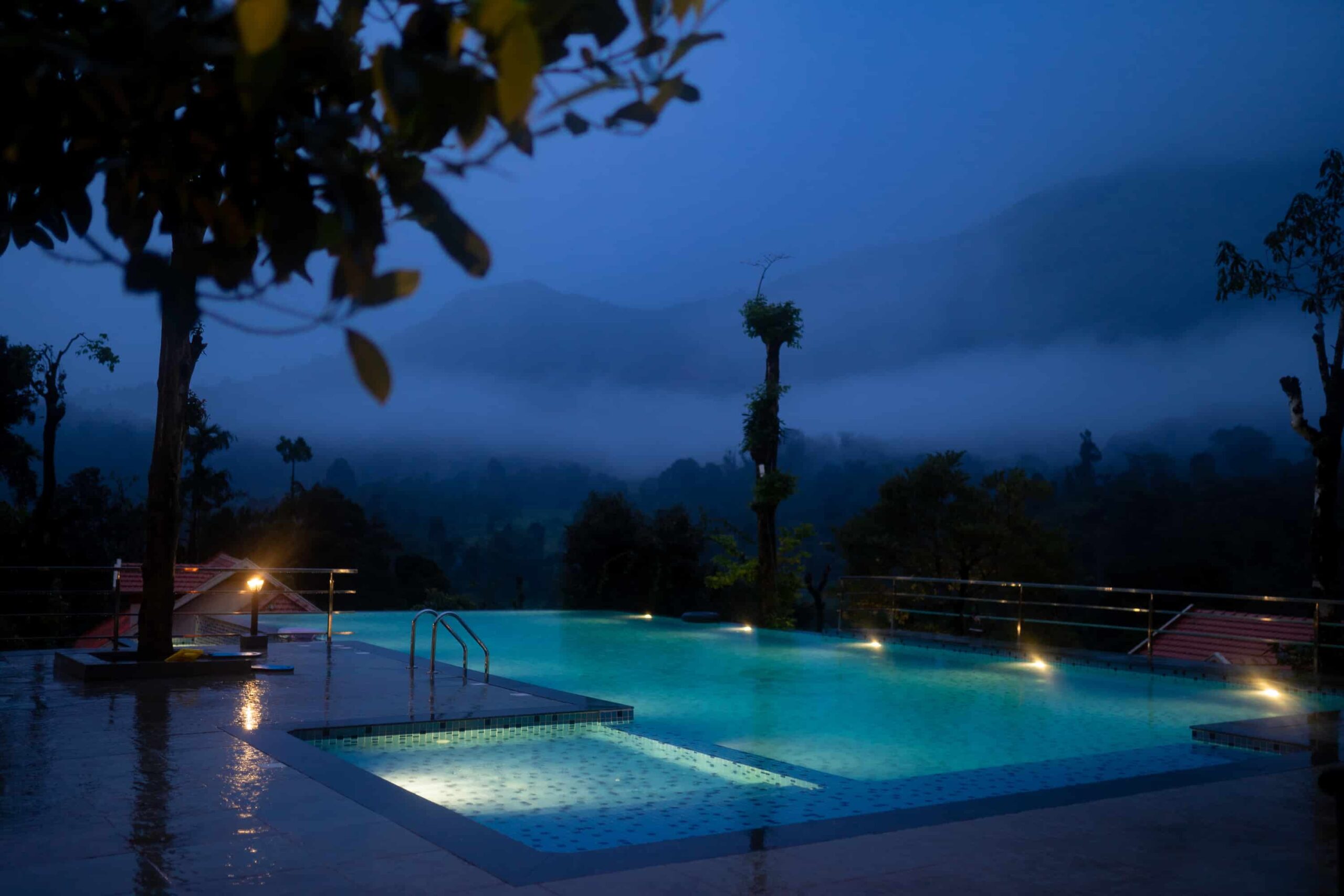 Lit infinity pool at dusk with mountain view. RiverMist Resorts.