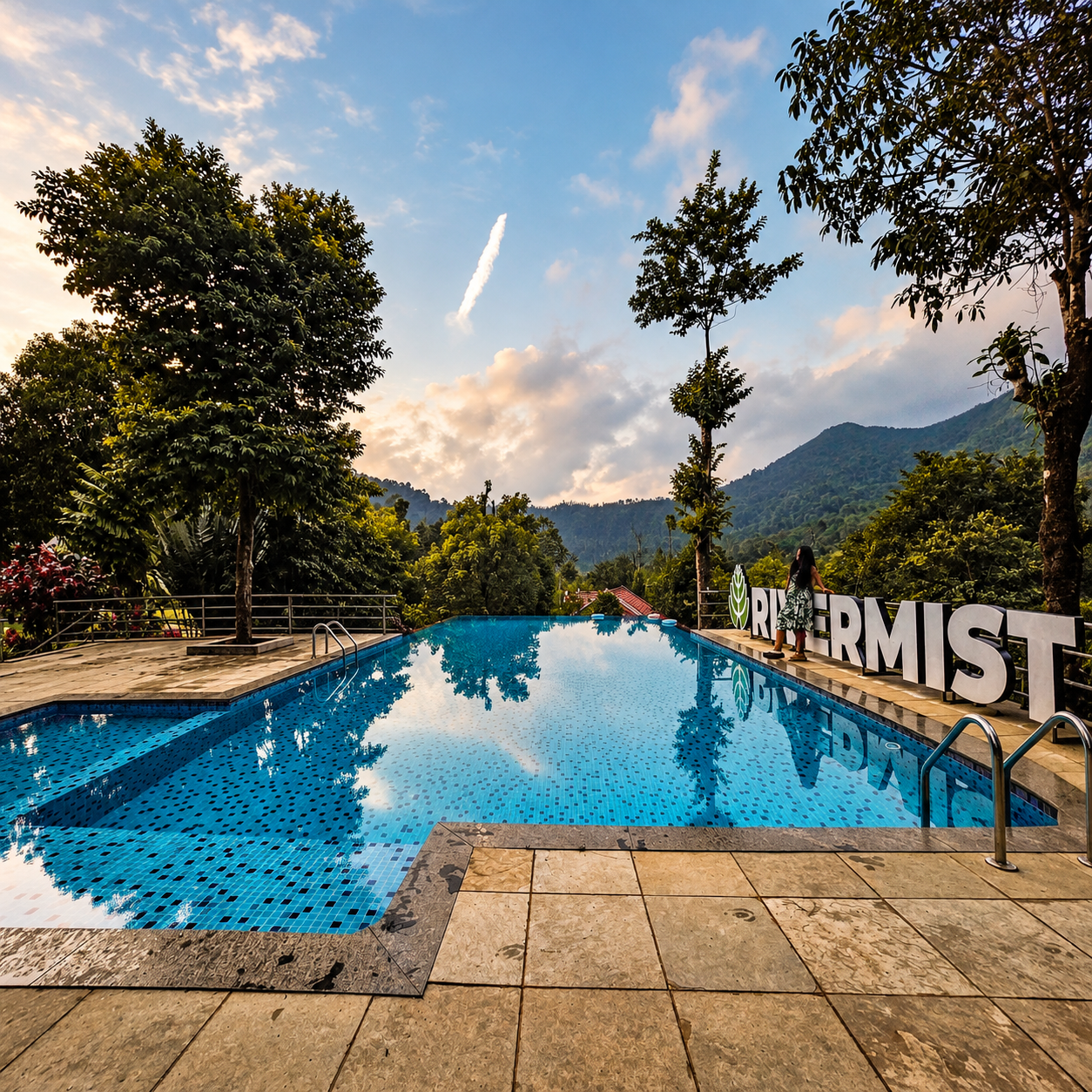 Infinity pool overlooking forested hills at RiverMist Resorts, with a guest beside the resort sign